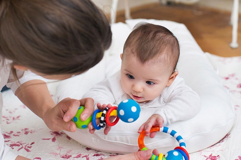 Bé nằm sấp vươn người về phía đồ chơi có âm thanh (Ảnh: sưu tầm internet).