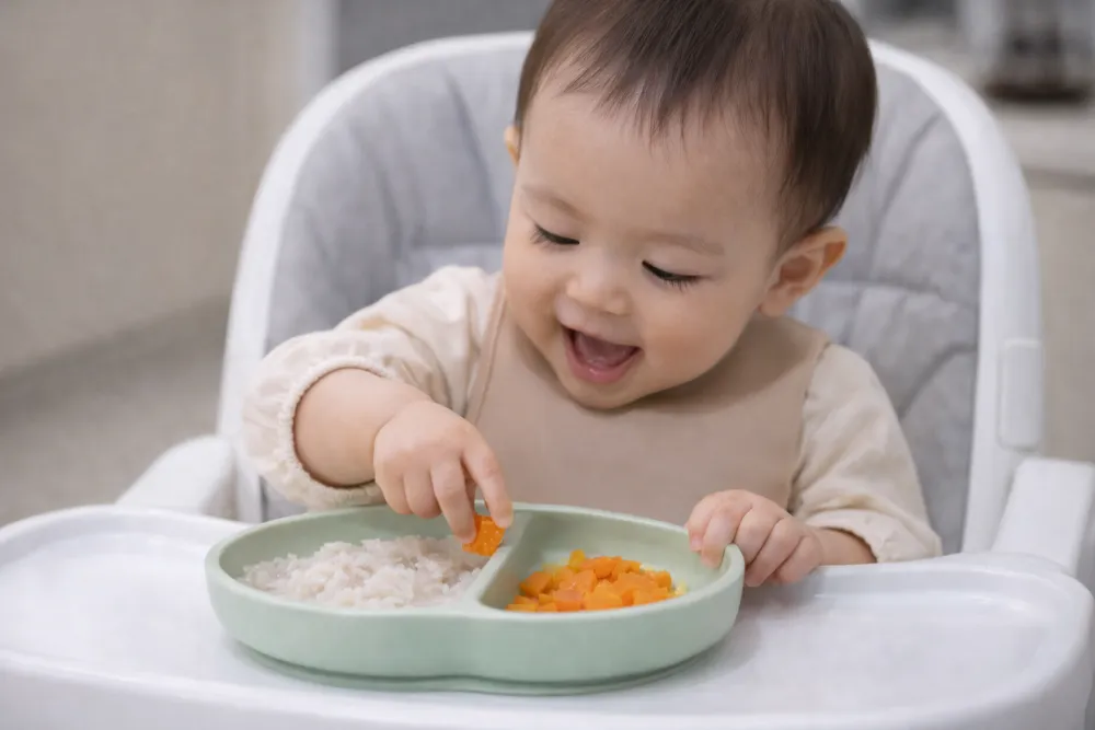 Bé 9 tháng hào hứng dùng hai ngón tay bốc nhón miếng cà rốt luộc trên khay ăn dặm