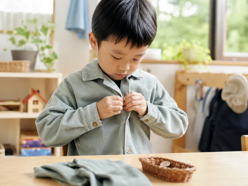 Tự cài cúc và mặc quần áo giúp trẻ rèn vận động tinh đồng thời hình thành kỹ năng tự phục vụ.